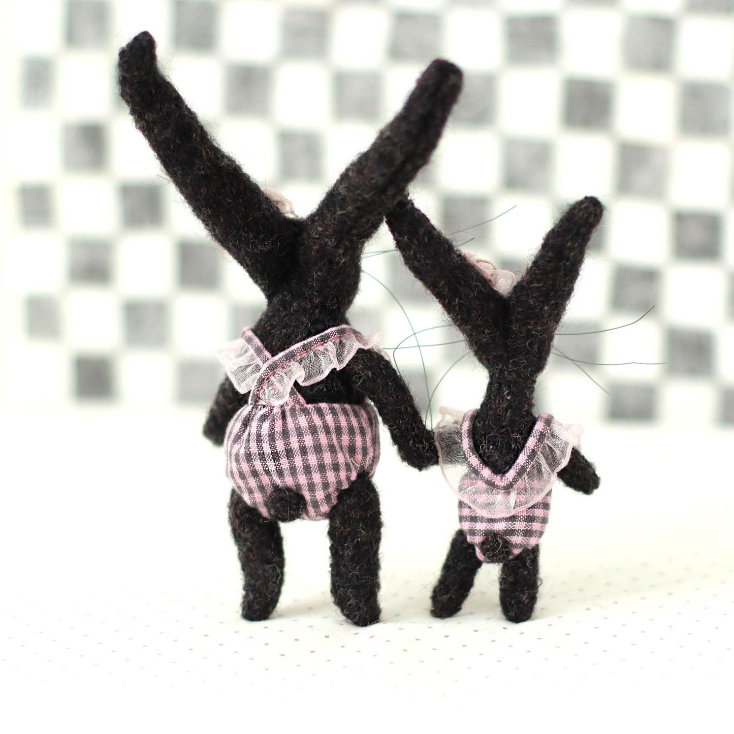 Handmade dark brown wool bunny collectible plush set — miniature rabbits in pink checked outfits, shown from the back, standing together with long upright ears