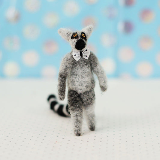 Hand-sewn miniature ring-tailed lemur plush toy with a striped tail and tiny bow tie, standing upright against a light blue background.