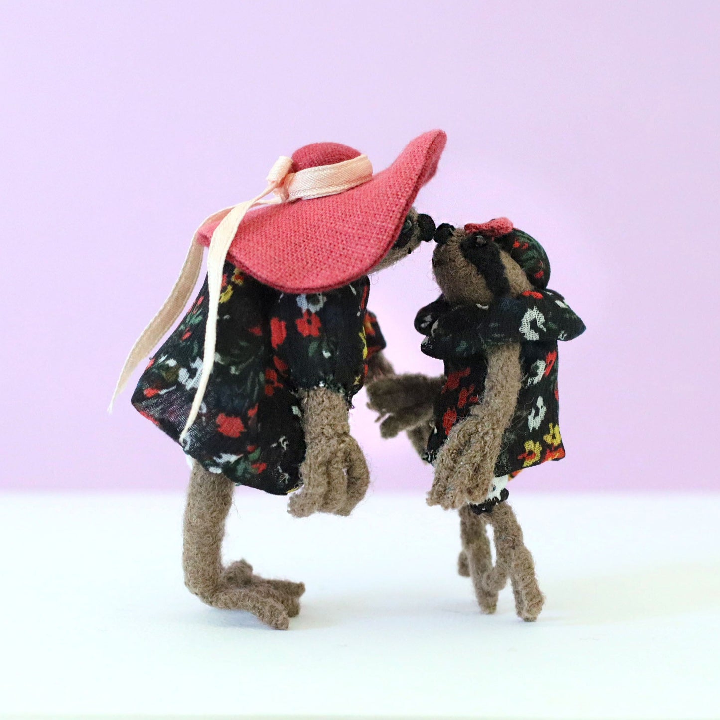 Handmade mama and baby sloth dolls in matching floral dresses, touching noses against a soft pink background