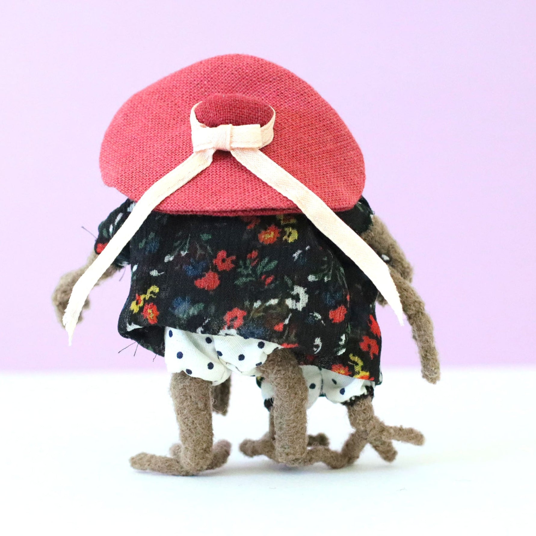 Handmade sloth mother and daughter dolls standing together from behind, both in black floral dresses, with the mama sloth wearing a large pink hat tied with a bow