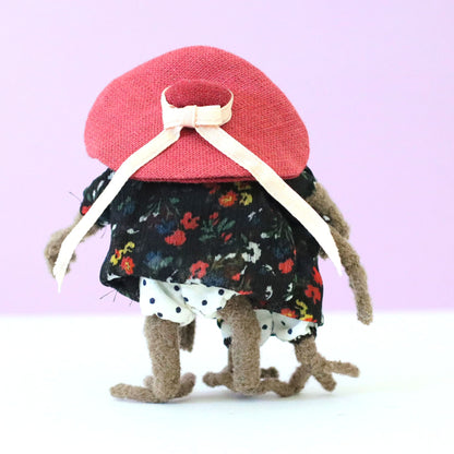 Handmade sloth mother and daughter dolls standing together from behind, both in black floral dresses, with the mama sloth wearing a large pink hat tied with a bow