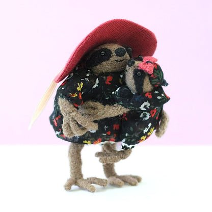 Handmade mama sloth doll in a pink sun hat holding her baby, both dressed in matching black floral dresses, posed against a soft pastel background