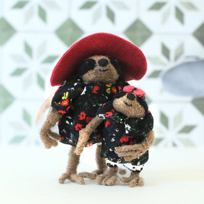 Handcrafted mama sloth doll wearing a red sun hat standing beside her baby sloth, both dressed in matching black floral outfits, posed against a patterned tile background