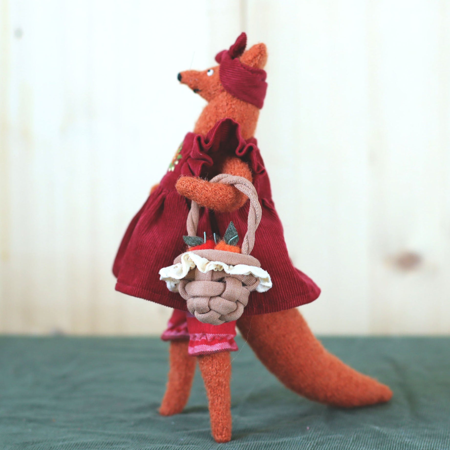 Handmade fox doll in a red dress and headband, holding a small woven basket filled with felt apples
