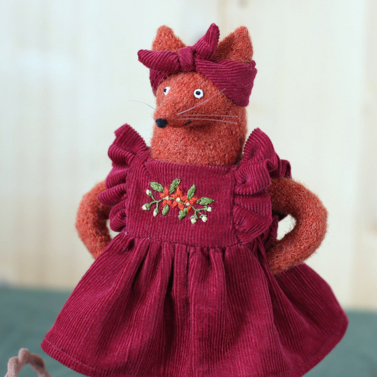 Handmade fox doll wearing a deep red corduroy dress with embroidered flowers and a matching headband