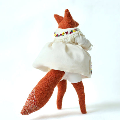 Handmade fox doll shown from the back, wearing a cream embroidered dress with lace trim, revealing orange textured legs and a bushy fox tail