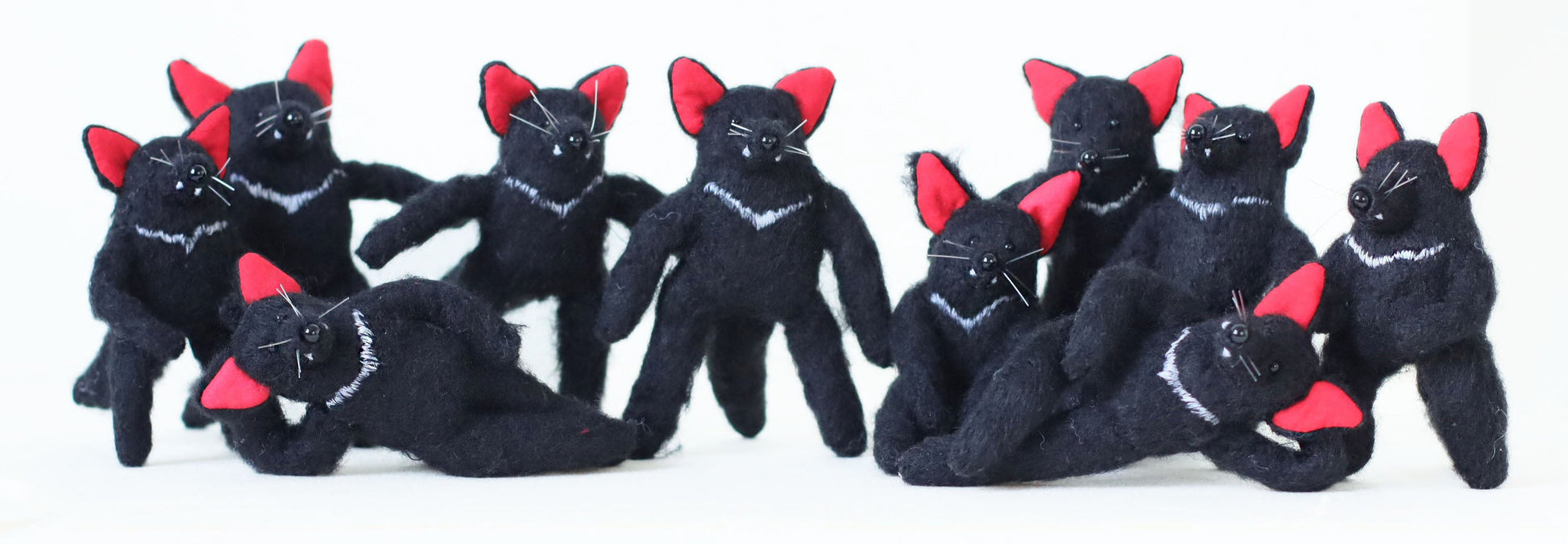 Large group of handmade Tasmanian devil plush toys with black fur, red ears, and white chest markings, posing together.