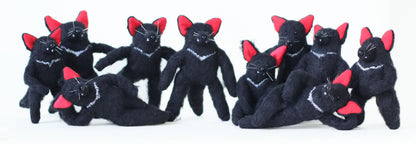 Large group of handmade Tasmanian devil plush toys with black fur, red ears, and white chest markings, posing together.