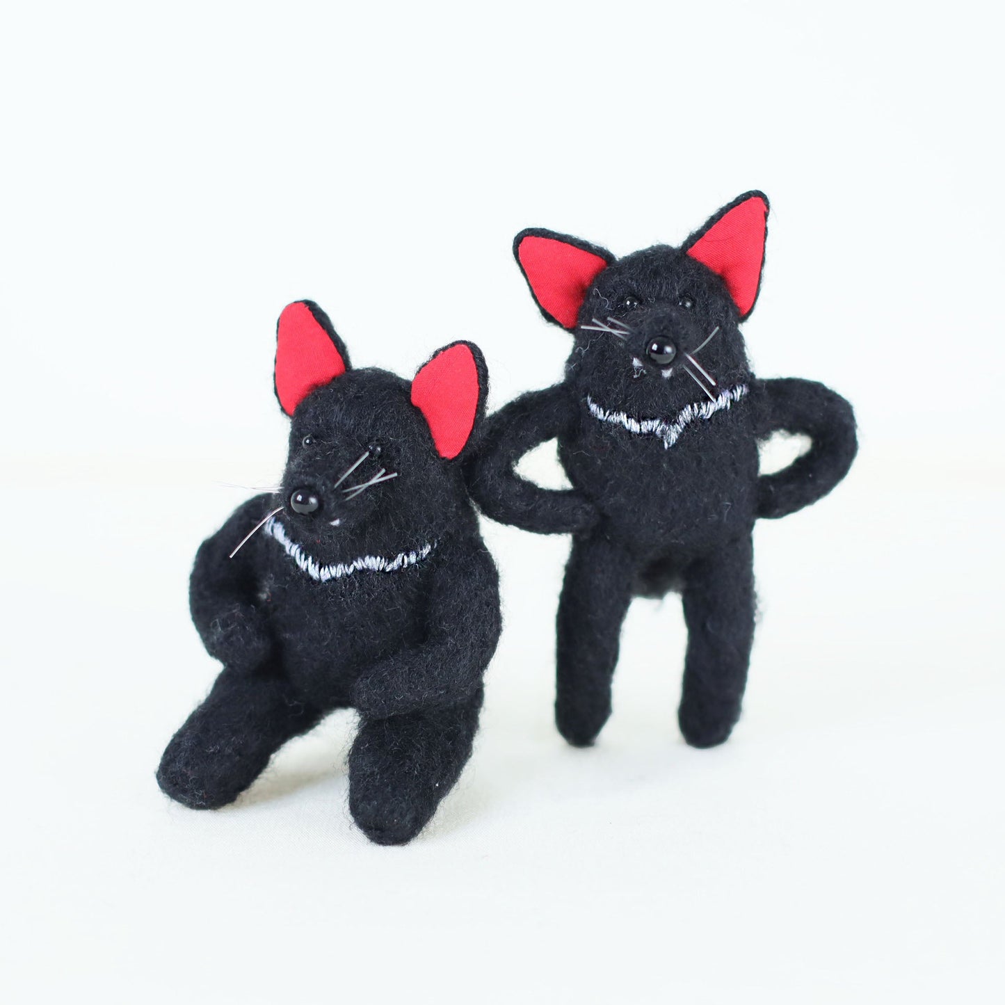 Pair of artisan Tasmanian devil plush dolls, one sitting and one standing, featuring black fur, red ears, and embroidered white chest details.