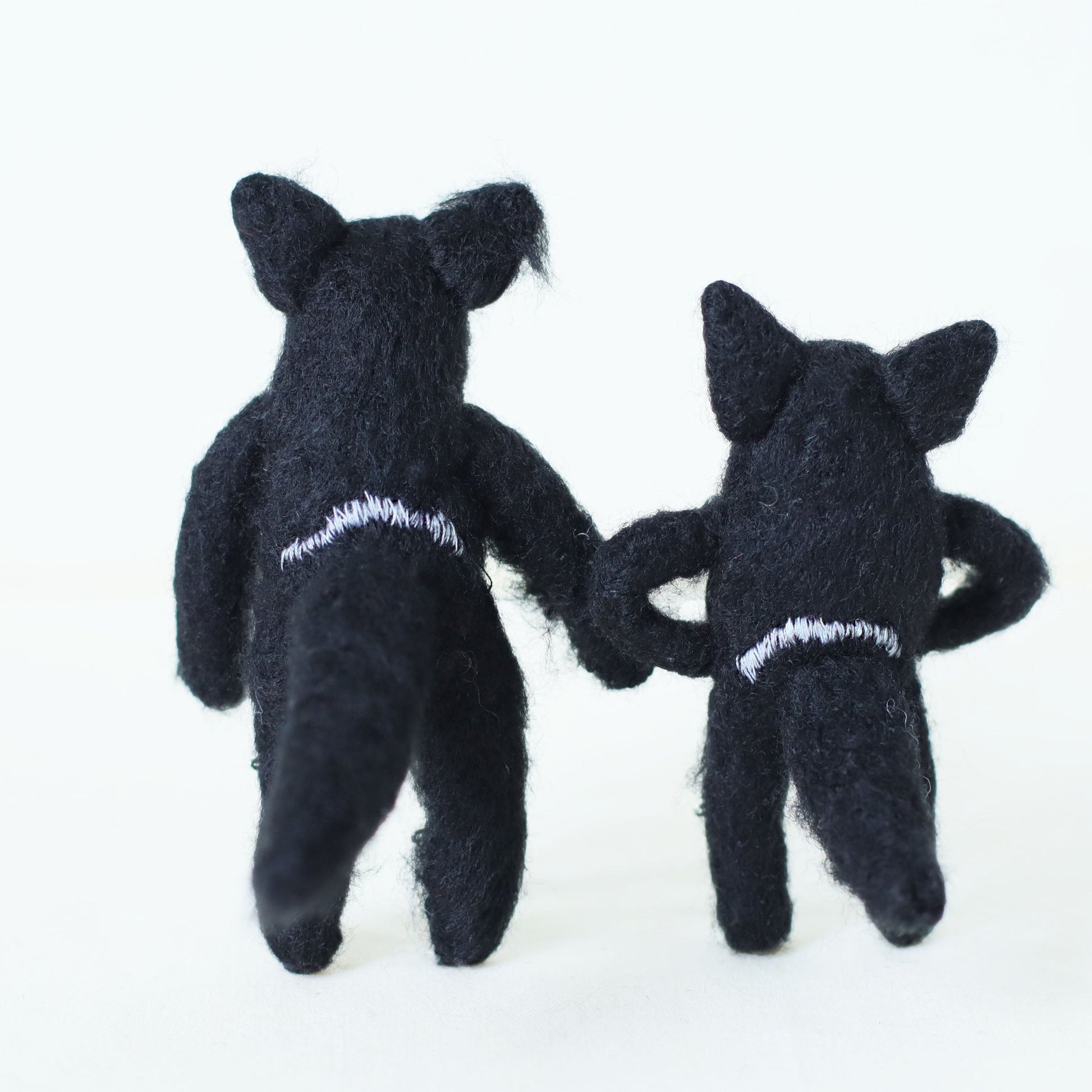 Pair of handmade Tasmanian devil plush dolls standing with their backs toward the viewer, showing soft black fur and embroidered details.
