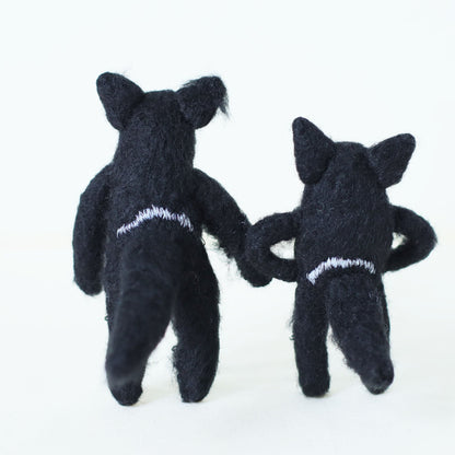 Pair of handmade Tasmanian devil plush dolls standing with their backs toward the viewer, showing soft black fur and embroidered details.