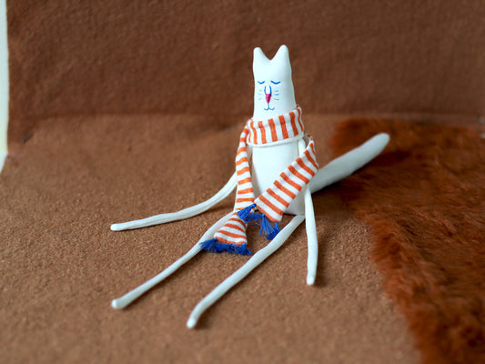 Handmade white cat plush toy with long legs, sitting on the floor with an orange striped scarf