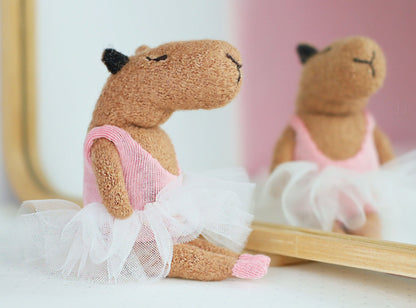 Handmade miniature capybara ballerina doll sitting in front of a mirror, wearing a pink leotard, white tulle tutu, and tiny pink ballet shoes