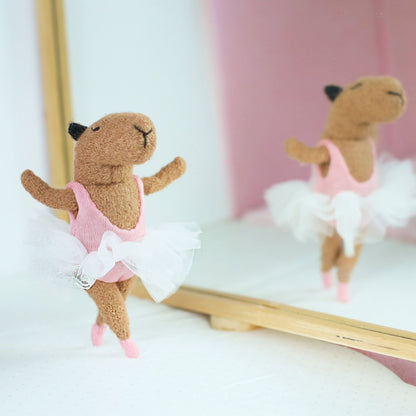 Handmade miniature capybara ballerina doll dancing in front of a mirror, wearing a pink leotard, white tulle tutu, and tiny pink ballet shoes
