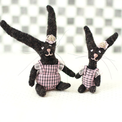 andmade dark brown wool bunny collectible plush set — miniature rabbits in pink checked outfits with floral headpieces, sitting and standing together.
