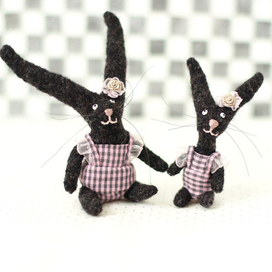 andmade dark brown wool bunny collectible plush set — miniature rabbits in pink checked outfits with floral headpieces, sitting and standing together.