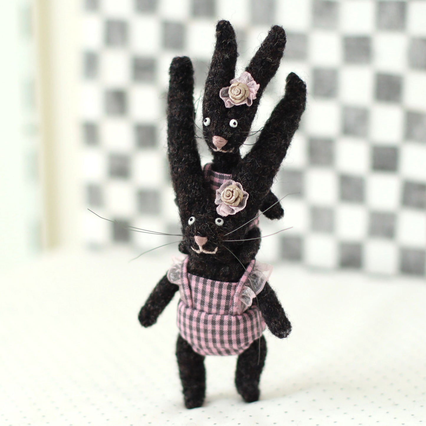 Handmade dark brown wool bunny collectible plush set — miniature rabbits in pink checked outfits with floral headpieces, posed with the baby bunny riding on the adult’s shoulders.