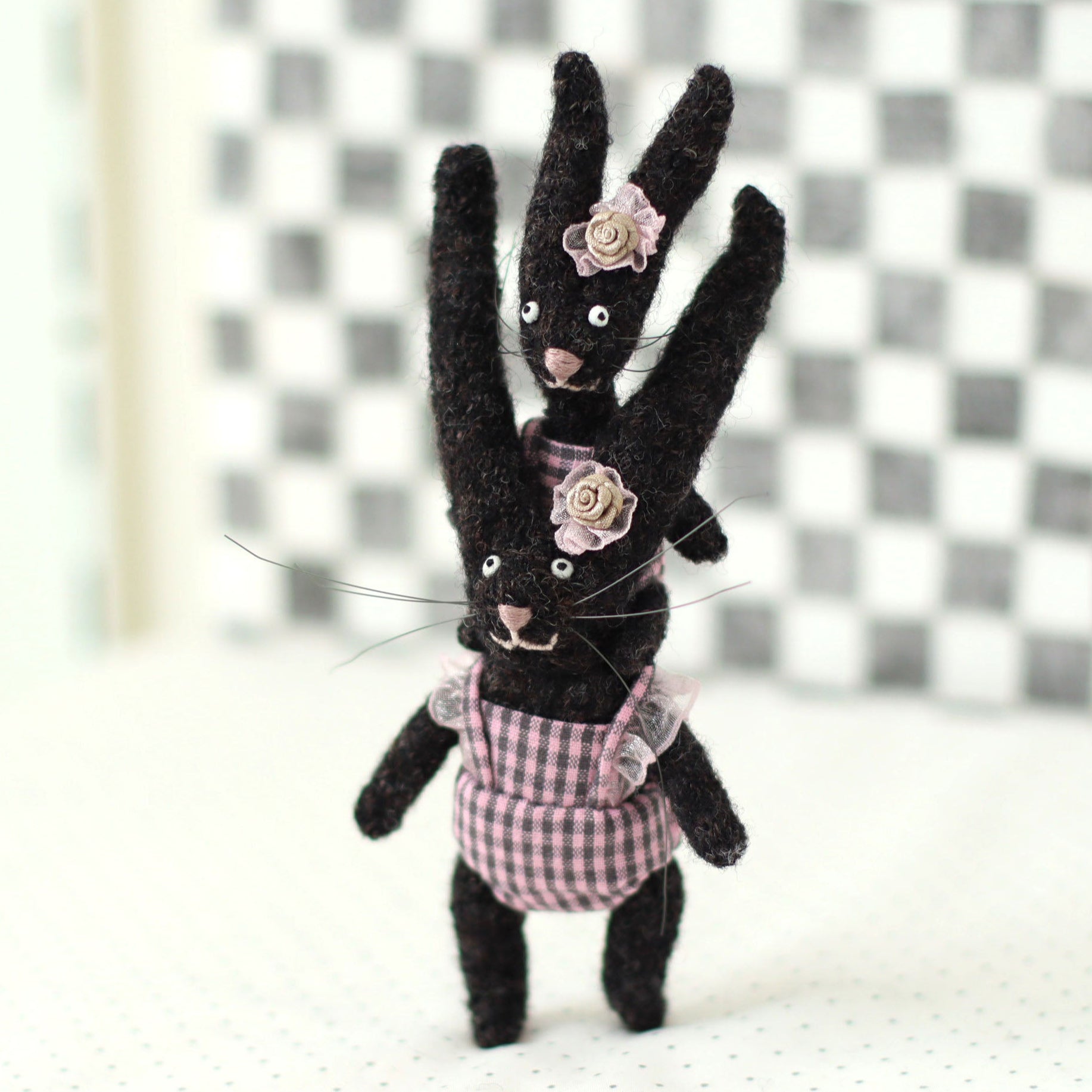 Handmade dark brown wool bunny collectible plush set — miniature rabbits in pink checked outfits with floral headpieces, posed with the baby bunny riding on the adult’s shoulders.
