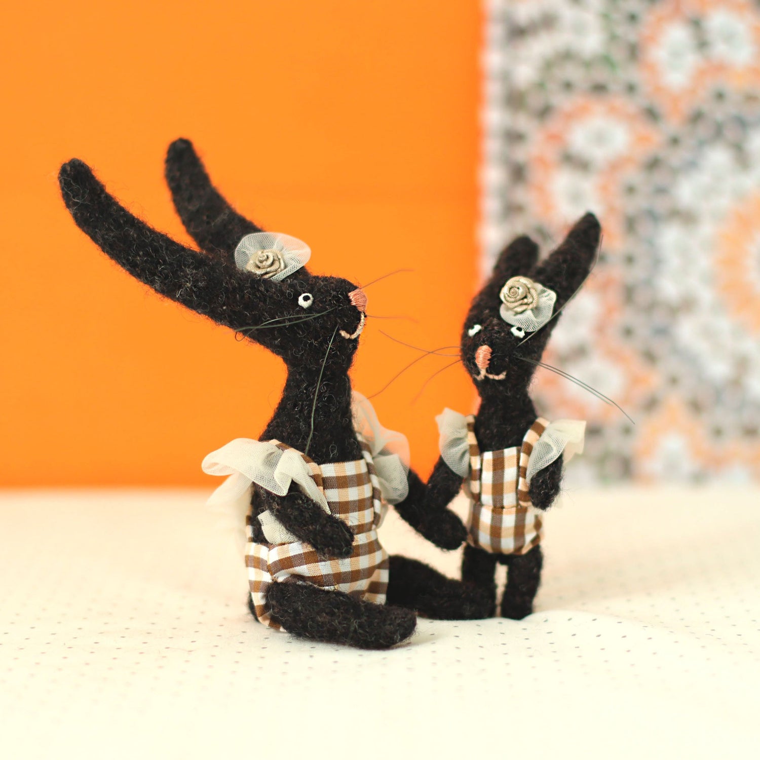 Handmade black bunny collectible plush set — miniature soft sculpture rabbits in gingham outfits with floral headpieces, sitting and standing together.