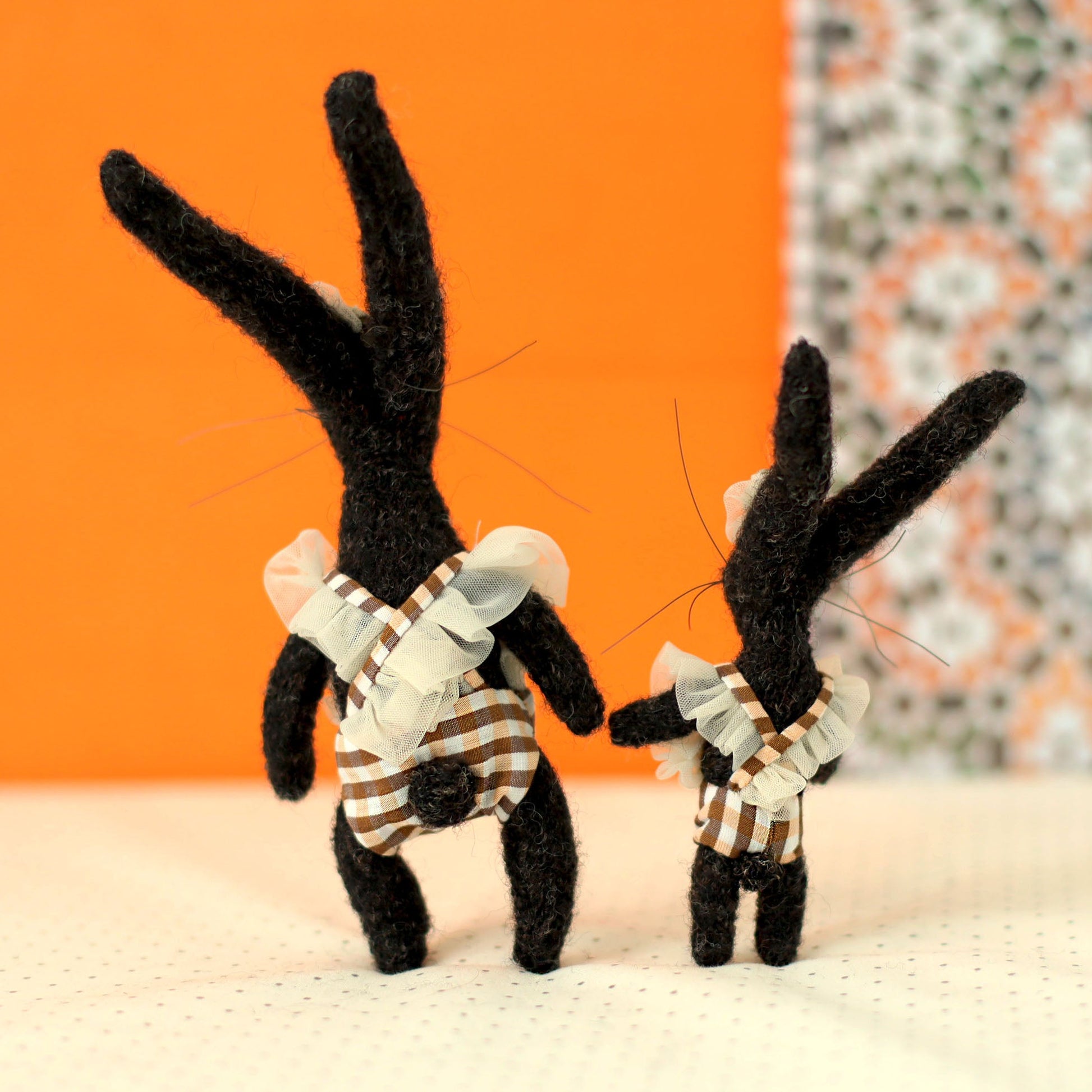 Handmade black bunny collectible plush set — mother and daughter rabbits in matching checked outfits with ruffled straps, viewed from the back, standing side by side with ears raised and holding hands