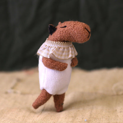 Profile view of a tiny capybara art doll with closed eyes, a beige ruffle collar, and white romper on a natural linen background