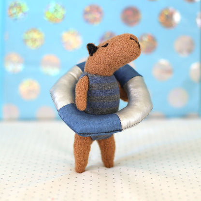 Miniature handmade capybara doll in a blue striped swimsuit standing inside a small blue-and-white float ring