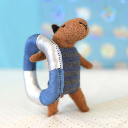 Mini handmade capybara doll wearing a blue striped swimsuit and holding a blue-and-silver float ring
