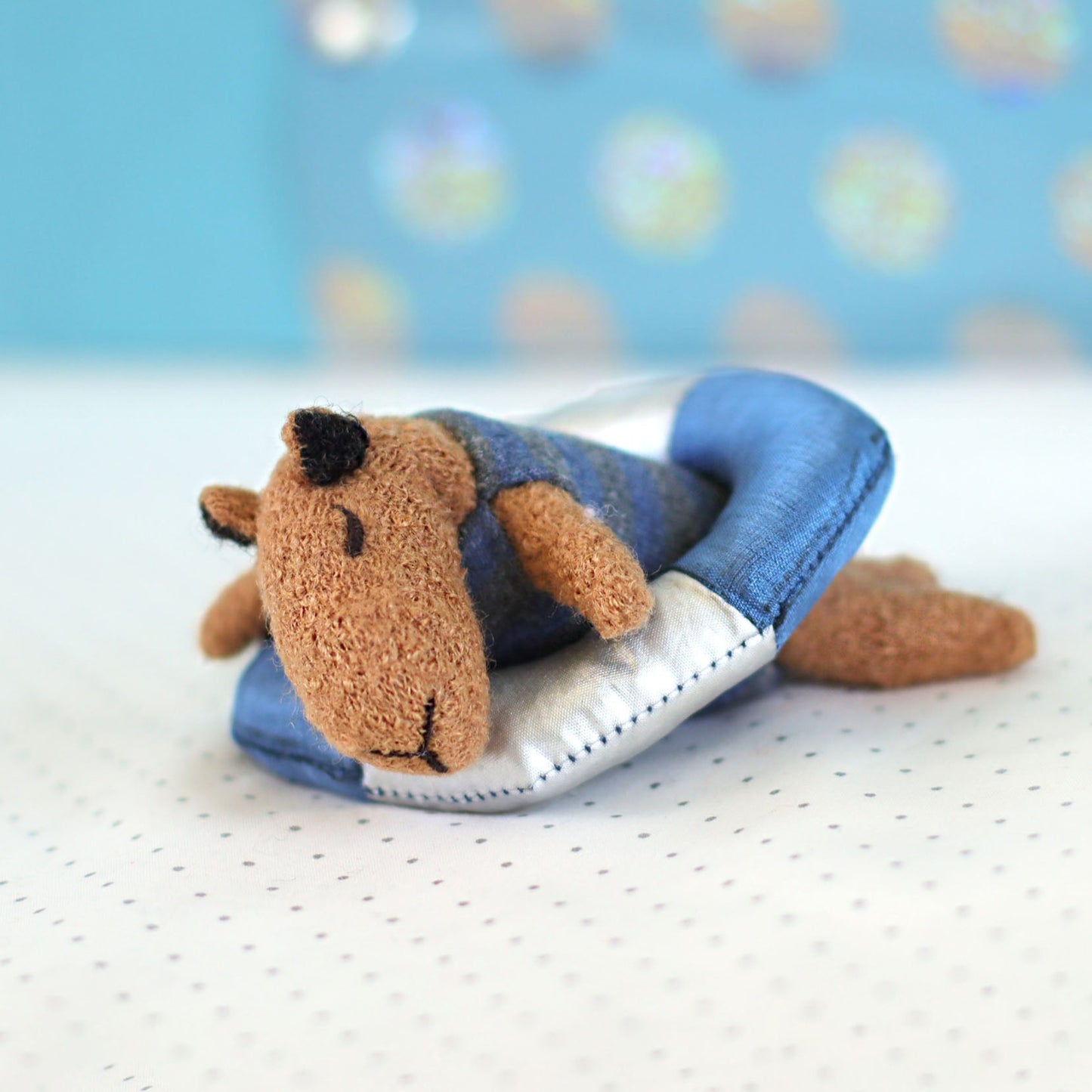 Mini handmade capybara doll lying on a tiny blue and silver float ring