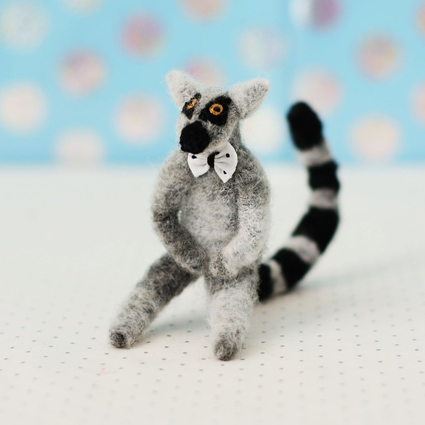 Hand-sewn miniature ring-tailed lemur plush toy with a bow tie and black-and-white striped tail, sitting in a relaxed pose.