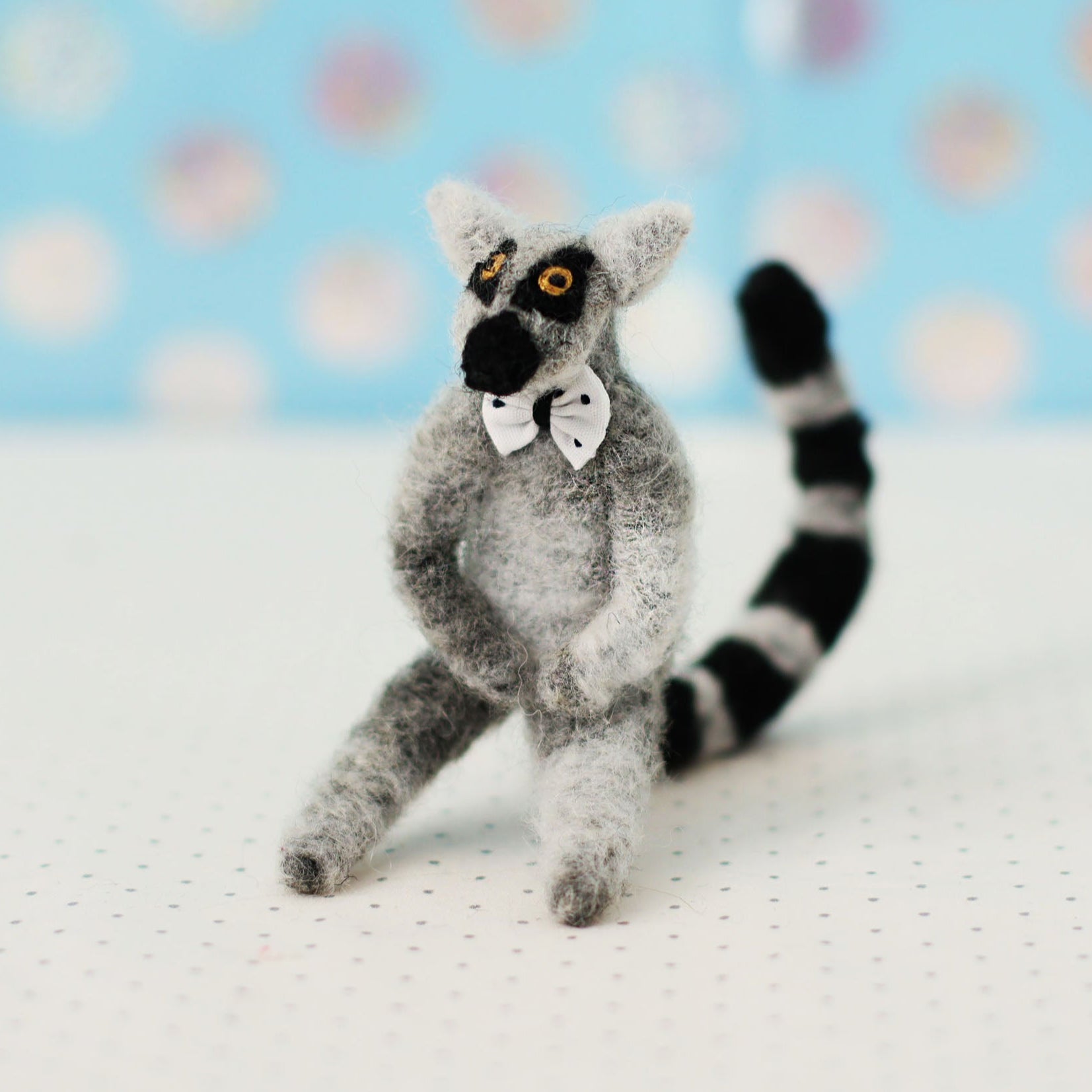 Hand-sewn miniature ring-tailed lemur plush toy with a bow tie and black-and-white striped tail, sitting in a relaxed pose.