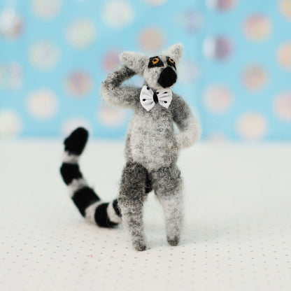 Handmade ring-tailed lemur collectible plush — miniature soft sculpture with striped tail and bow tie, standing in a playful pose with one hand on its head.