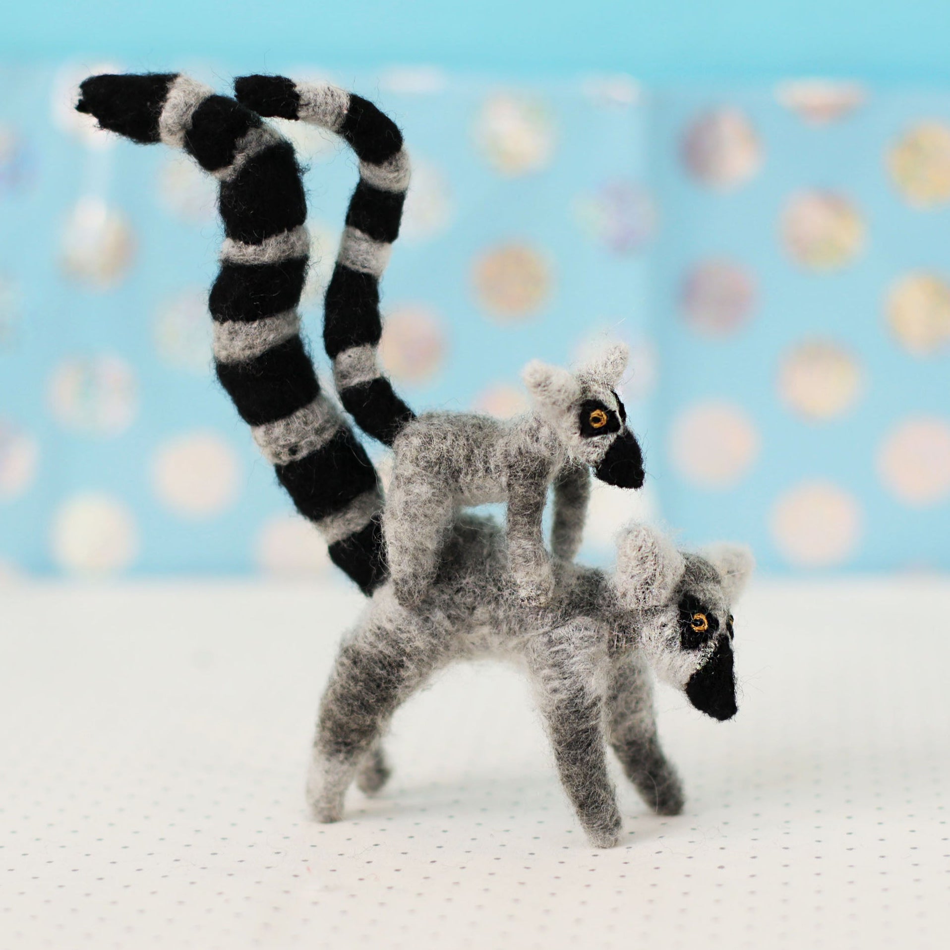 Two toy lemurs with black and white striped tails on a light blue background with polka dots.