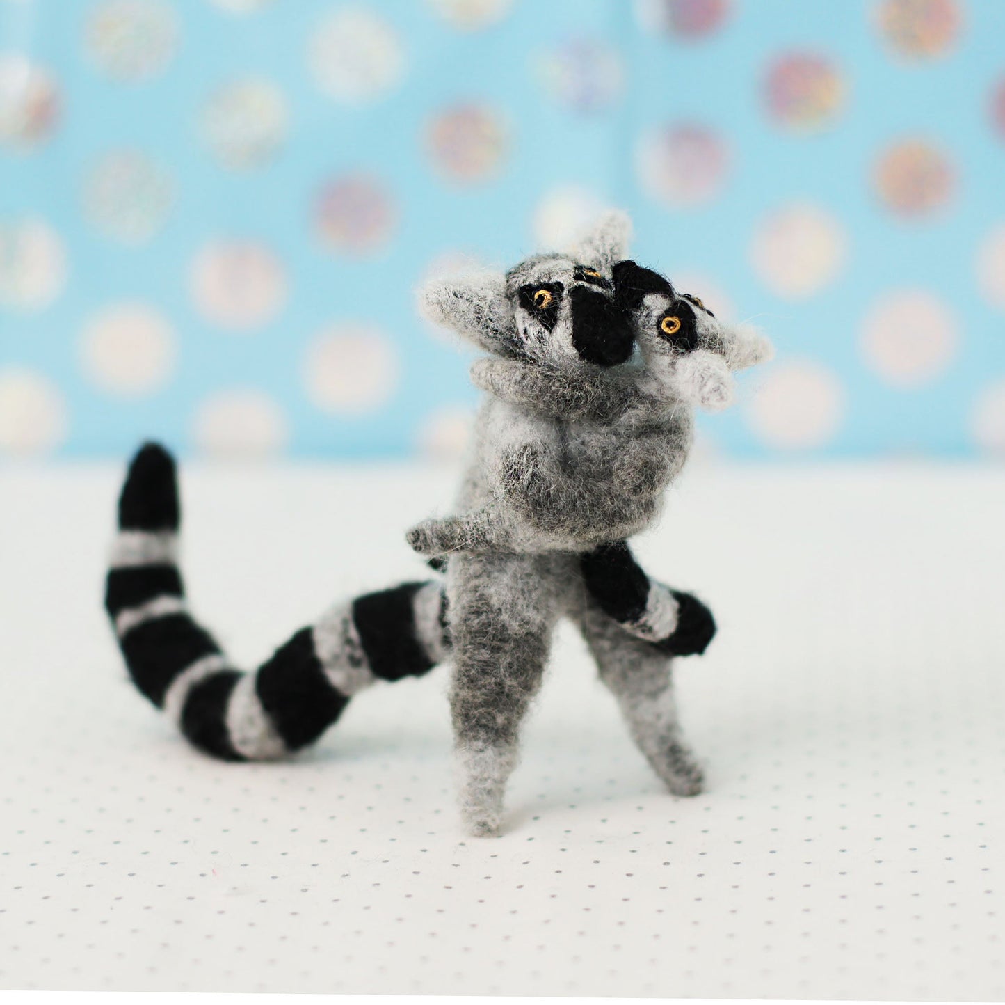 Hand-sewn miniature ring-tailed lemur plush toys hugging each other, with gray fur, black-and-white striped tails, and expressive embroidered faces.