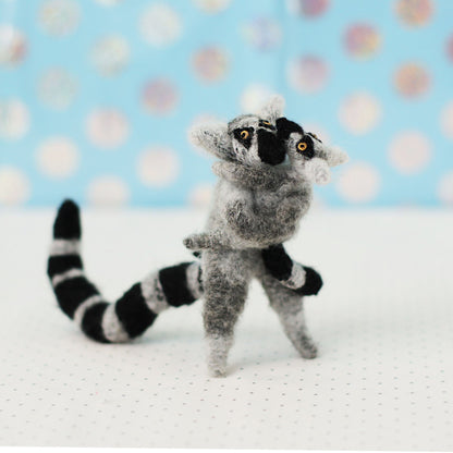 Hand-sewn miniature ring-tailed lemur plush toys hugging each other, with gray fur, black-and-white striped tails, and expressive embroidered faces.