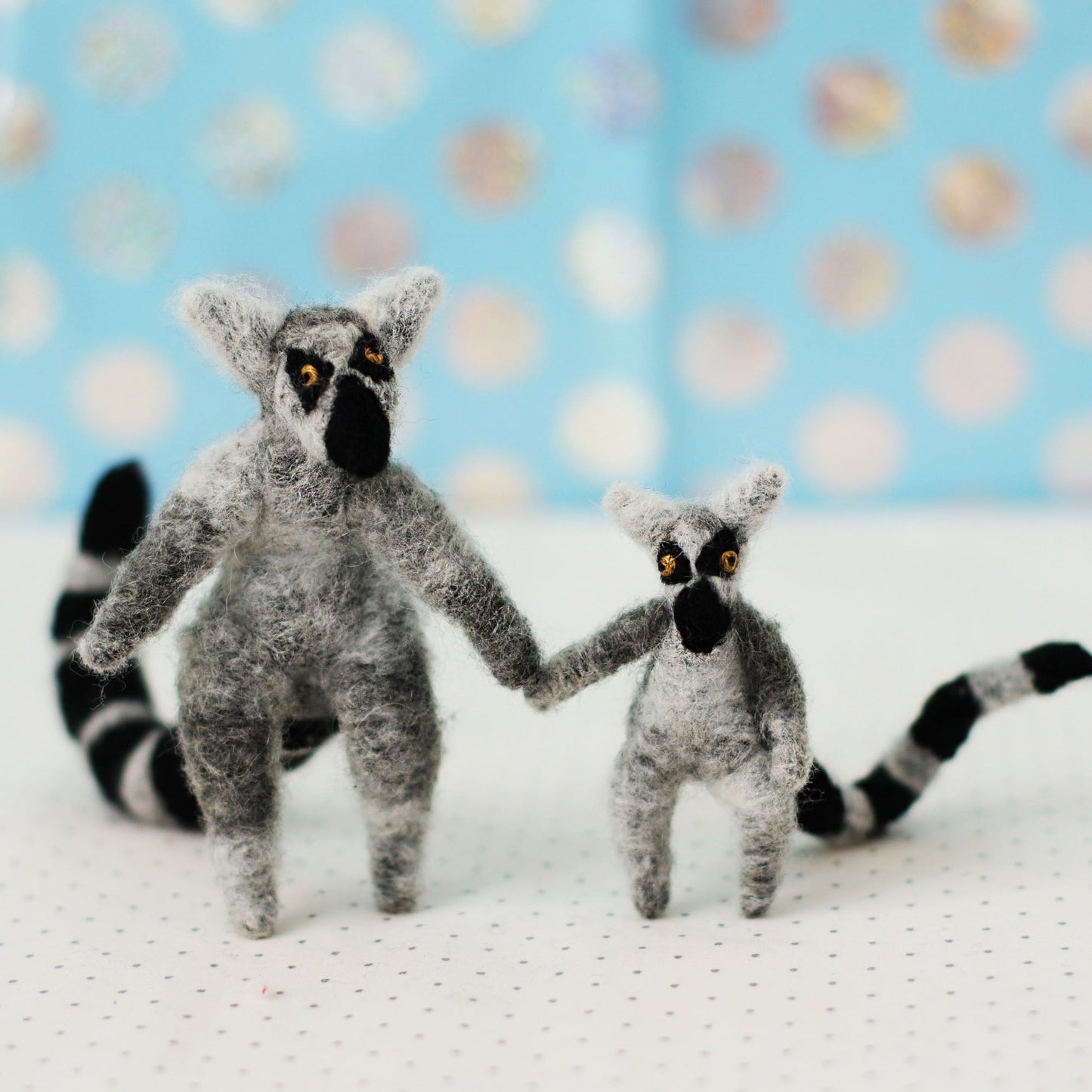 Two hand-sewn miniature ring-tailed lemur plush toys with black-and-white striped tails, standing side by side and holding hands.